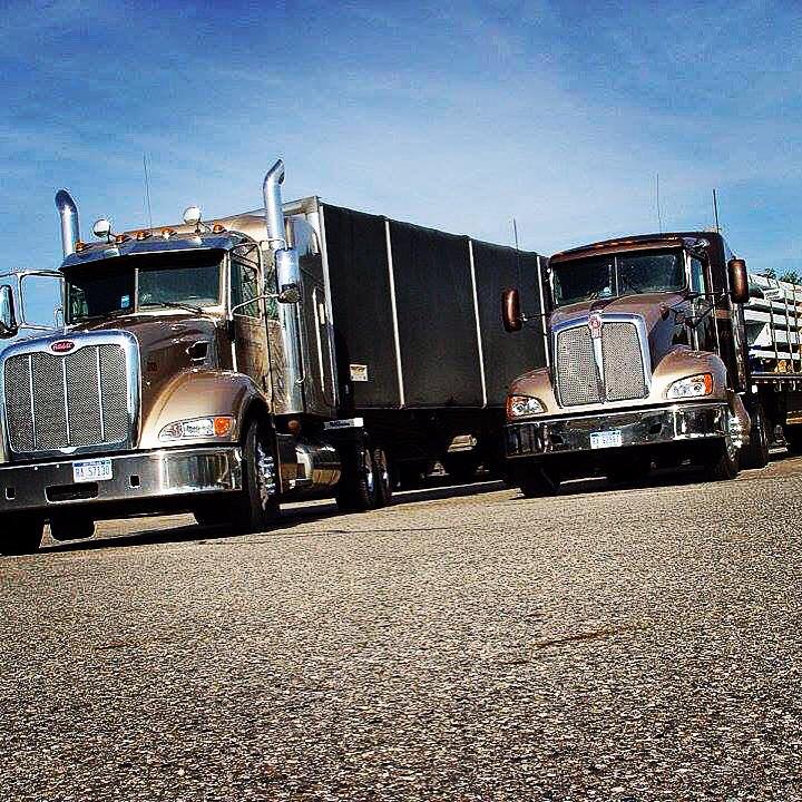 680f86d24df3f_OPENCON Two semi trucks parked in a lot on the side of road.